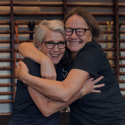 Two elderly women hugging each other in a gym.